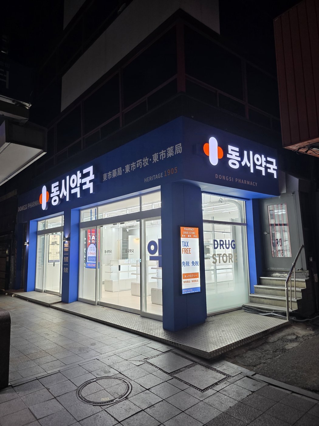 Dongsi Pharmacy storefront at night: a blue facade with the white 동시약국 sign